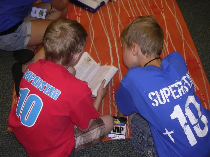 Two kids in Go Fish VBS shirts reading the Bible together